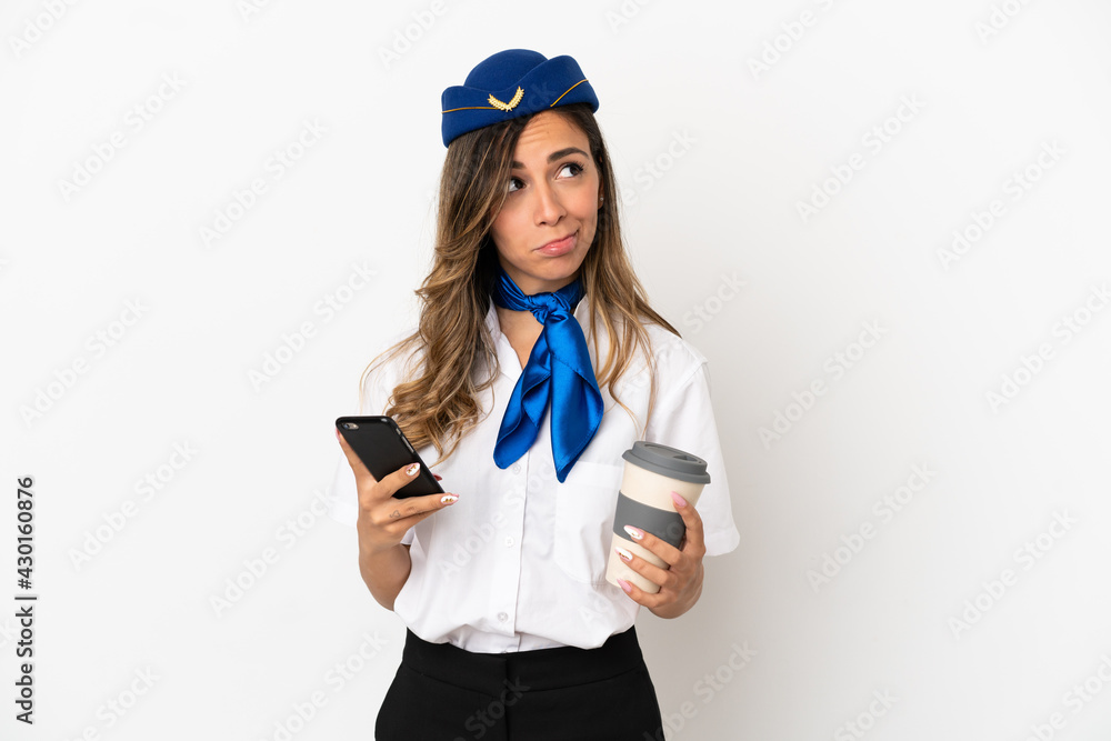 Airplane stewardess over isolated white background holding coffee to take away and a mobile while thinking something Airplane stewardess over isolated white background holding coffee to take away and a mobile while thinking something