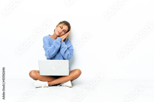 Young blonde Uruguayan girl with the laptop isolated on white background making sleep gesture in dorable expression