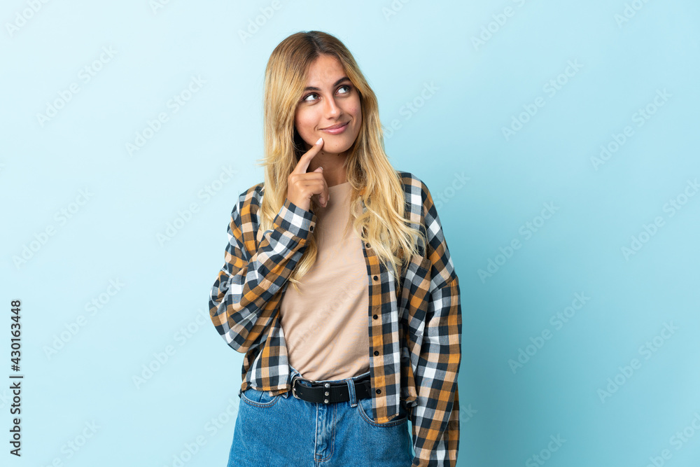 Young blonde Uruguayan isolated on blue background and looking up