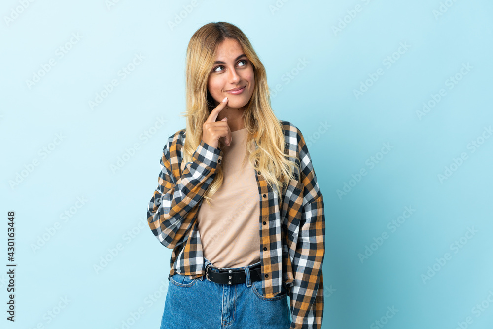 Young blonde Uruguayan isolated on blue background and looking up Young blonde Uruguayan isolated on blue background and looking up