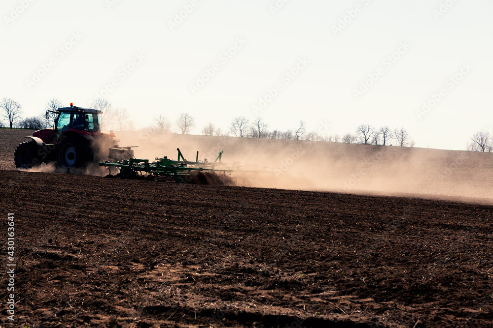 Fototapeta premium Tractor Plowing Agricultural Field in the Spring . Dust over the agricultural field