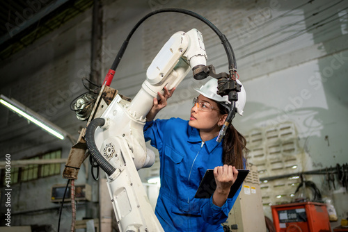 Technician woman check the robotic arm machine in the factory. Worker wearing safety helmet, glasses and uniform. Preventive maintenance to prevent breakdown. Service and repair concept photo