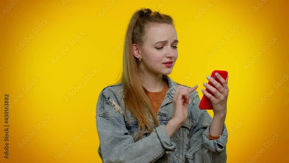 Teen stylish girl in denim jacket use mobile cell phone typing browsing, loses becoming surprised sudden lottery results, bad fortune, loss. Young woman on yellow background. People sincere emotions Teen stylish girl in denim jacket use mobile cell phone typing browsing, loses becoming surprised sudden lottery results, bad fortune, loss. Young woman on yellow background. People sincere emotions