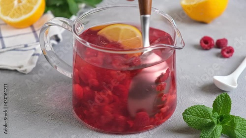 Raspberry tea with berries in glass teapot. Mixing raspberry tea with spoon. Concept of a healthy diet, vitamin breakfast