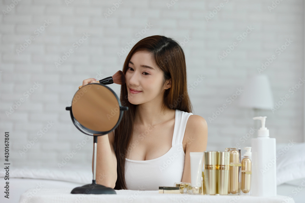 Happy Asian young woman smile and looking in mirror doing skin care applying make up brush on her cheek and beauty treatment at home,Wellness woman self care with beauty product at home Happy Asian young woman smile and looking in mirror doing skin care applying make up brush on her cheek and beauty treatment at home,Wellness woman self care with beauty product at home