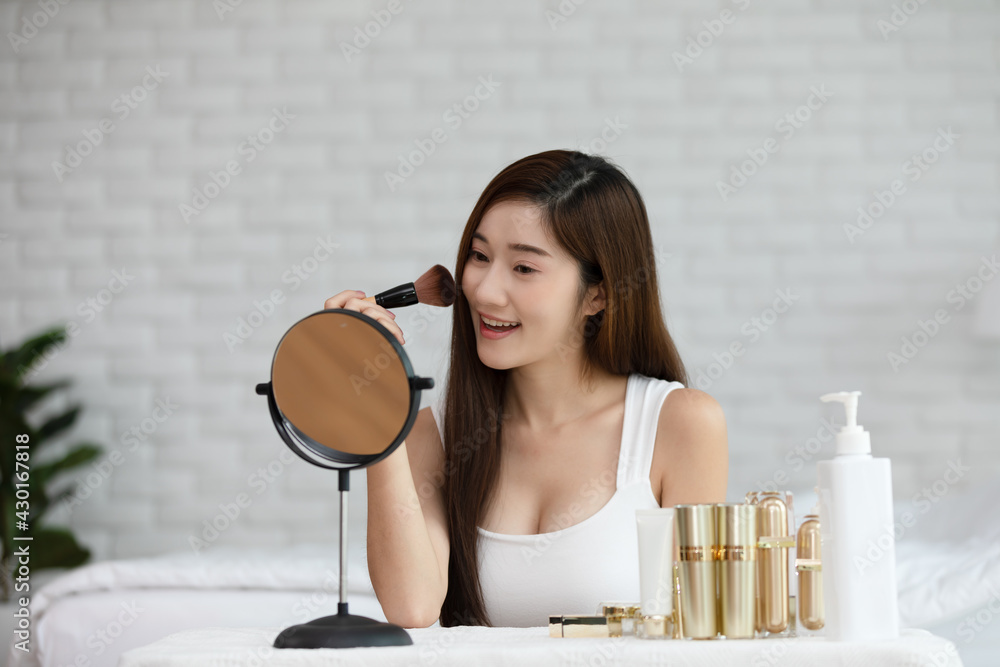 Happy Asian young woman smile and looking in mirror doing skin care applying make up brush on her cheek and beauty treatment at home,Wellness woman self care with beauty product at home Happy Asian young woman smile and looking in mirror doing skin care applying make up brush on her cheek and beauty treatment at home,Wellness woman self care with beauty product at home