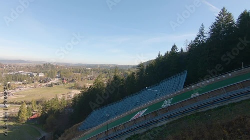 Family watching ski jumps training on Wielka Krokiew, Zakopane, Poland during autumn sunny day, slowmotion of flying jumper.