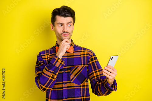 Photo of young thougtful minded curious man hold cellphone see interesting post isolated on yellow color background photo