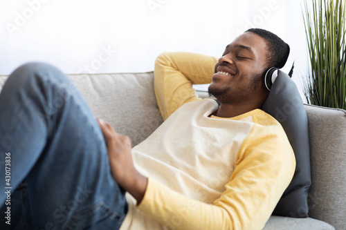 Happy african american guy enjoying music, using headset