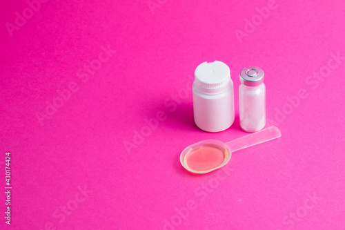 Ampoule with medicine, medicinal mixture and white jar of pills on pink background © queen1987