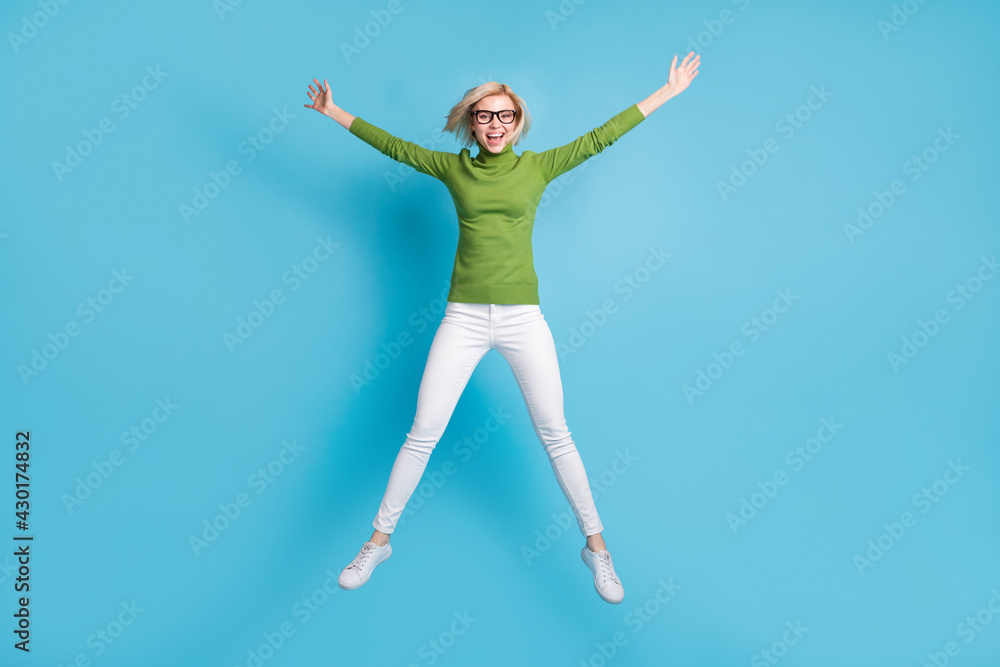 Full size photo of happy excited cheerful smiling girl in glasses jumping in star pose isolated on blue color background Full size photo of happy excited cheerful smiling girl in glasses jumping in star pose isolated on blue color background
