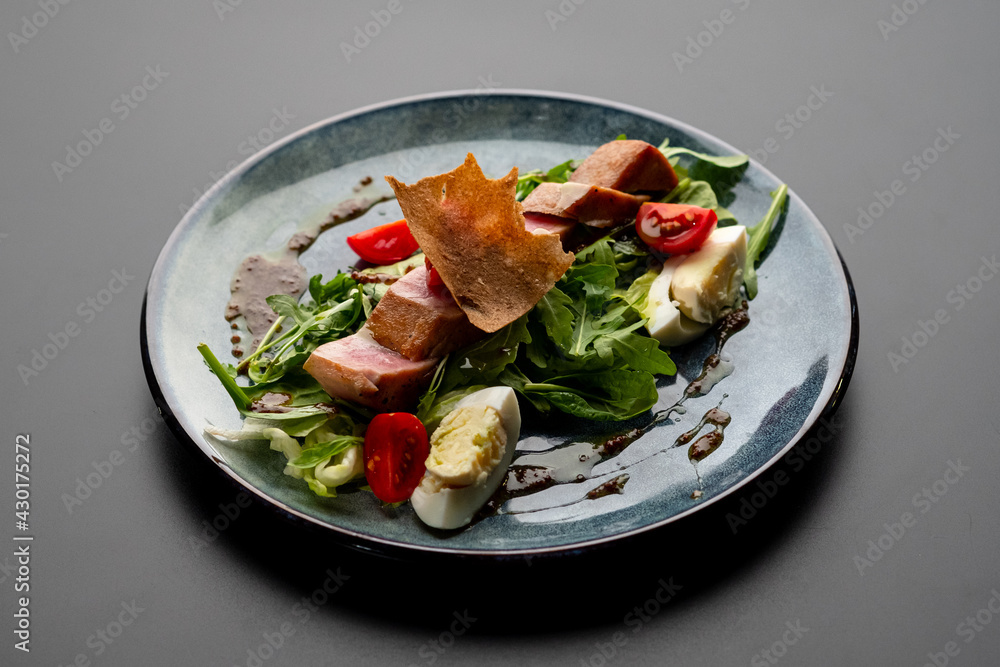 Meat salad with arugula and boiled egg on a gray plate on a black background. Restaurant menu. Meat salad with arugula and boiled egg on a gray plate on a black background. Restaurant menu.