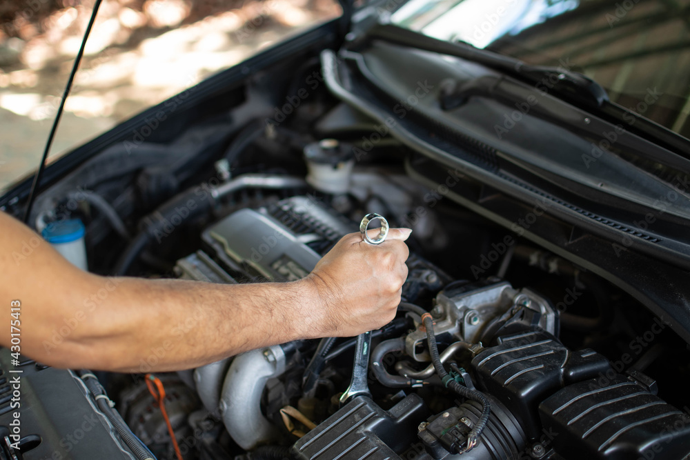 Concept of engine maintenance. Mechanics hold a wrench to tighten bolts in engine repairs. Black car, engine turned off. Engineers are checking the combustion system of cylinders. Blurred background Concept of engine maintenance. Mechanics hold a wrench to tighten bolts in engine repairs. Black car, engine turned off. Engineers are checking the combustion system of cylinders. Blurred background