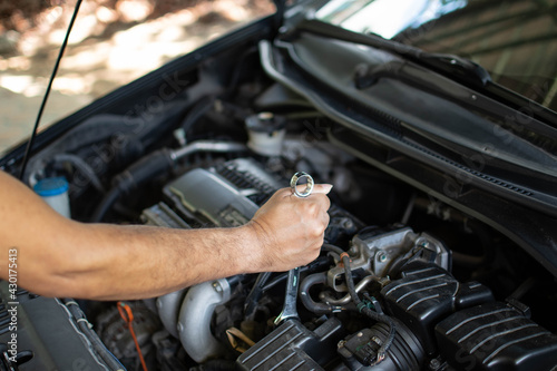 Concept of engine maintenance. Mechanics hold a wrench to tighten bolts in engine repairs. Black car, engine turned off. Engineers are checking the combustion system of cylinders. Blurred background