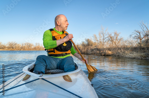 senior athletic male is paddling expedition canoe and watching wildlife on a shore, early spring scenery on a lake in northern Colorado, POV from boat bow