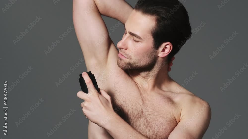 A confident man is using a body spray standing isolated over grey wall in the studio A confident man is using a body spray standing isolated over grey wall in the studio