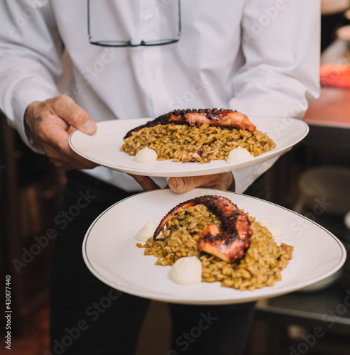 Camarero de un restaurante de lujo llevando dos platos gourmet de arroz con tentaculo de pulpo