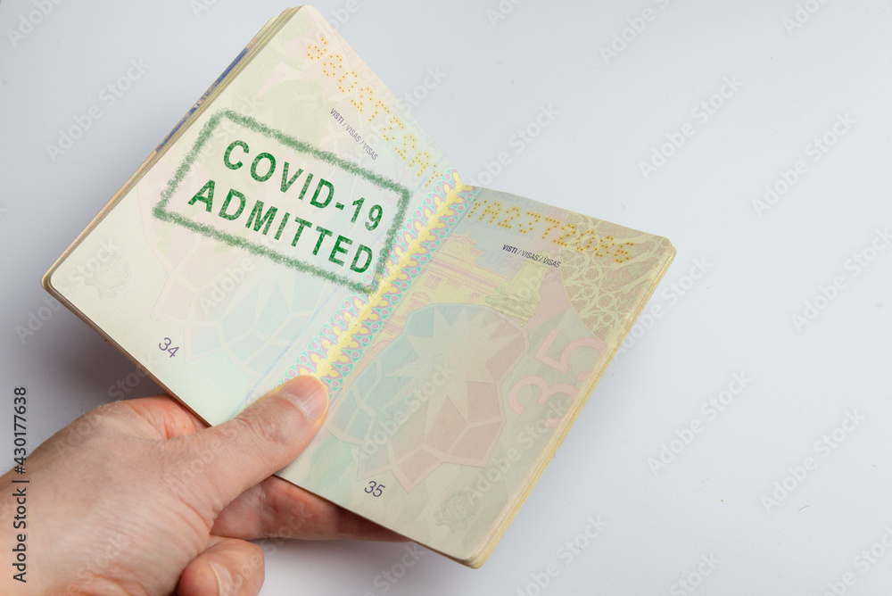 Concept representing a hand holding a vaccination passport with a stamp indicating that the passenger has been admitted: he is compliant with the vaccination requirements Concept representing a hand holding a vaccination passport with a stamp indicating that the passenger has been admitted: he is compliant with the vaccination requirements
