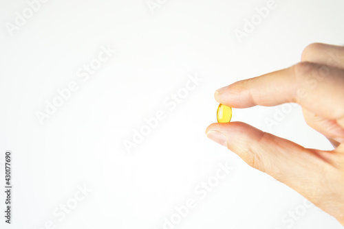 Close-up of a hand holding a yellow capsule full of vitamin D, used in homeopathy as well as in every treatment aimed at strenghten the immune system. White background.