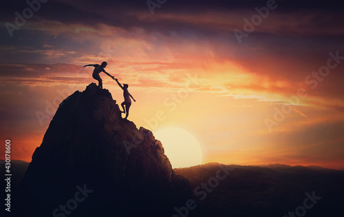 Scenery view with a team of two climbers on the top on the mountain. Person helping another to overcome obstacles and reach the top together. Teamwork concept, working in group to achieve success