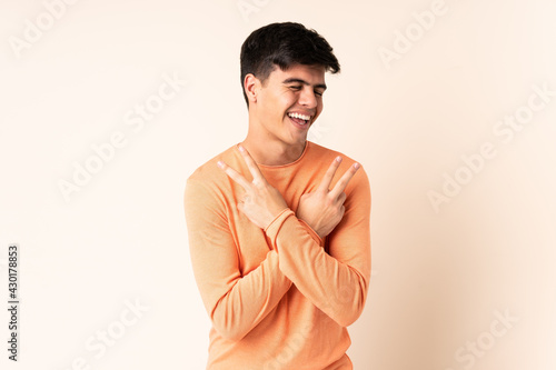 Handsome man over isolated beige background smiling and showing victory sign