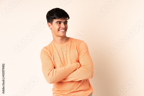 Handsome man over isolated beige background with arms crossed and happy