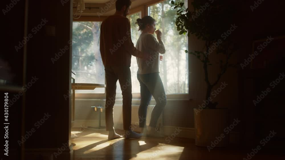 Couple At Home: Woman Watching Out of Window Male Partner Embraces Her From Behind. Happy Couple in Ideal Relationship Spending Sunny Day Together. Beautiful Family Moments Couple At Home: Woman Watching Out of Window Male Partner Embraces Her From Behind. Happy Couple in Ideal Relationship Spending Sunny Day Together. Beautiful Family Moments