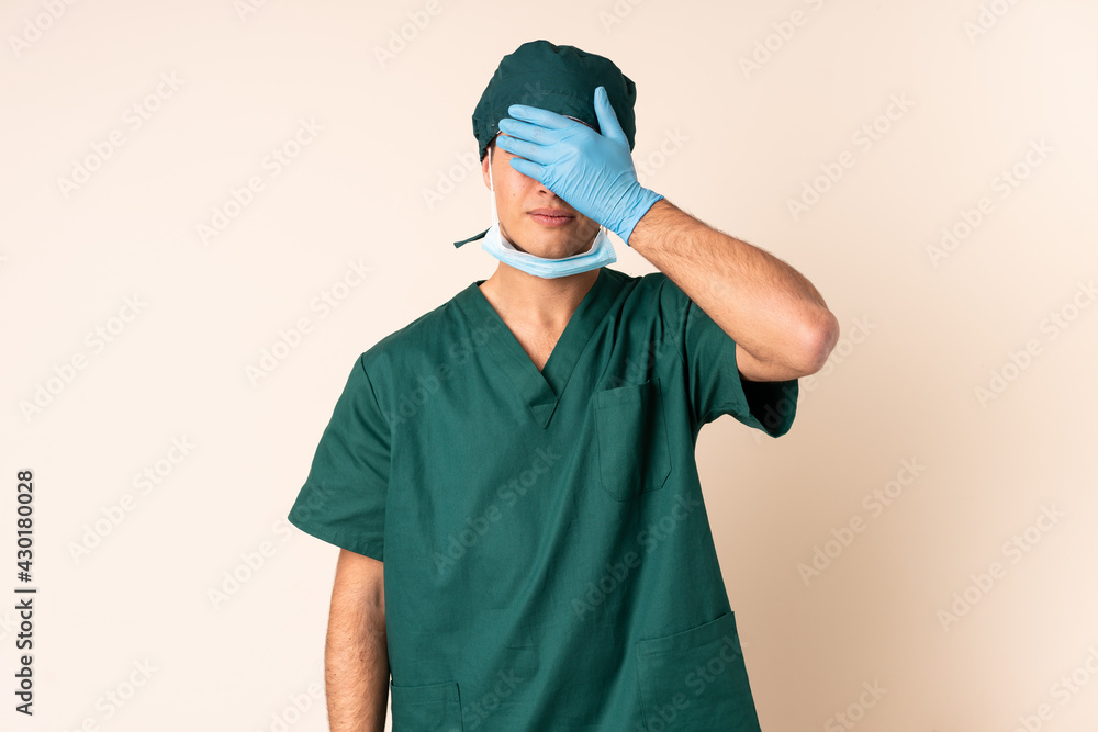 Surgeon man in blue uniform over isolated background covering eyes by hands Surgeon man in blue uniform over isolated background covering eyes by hands