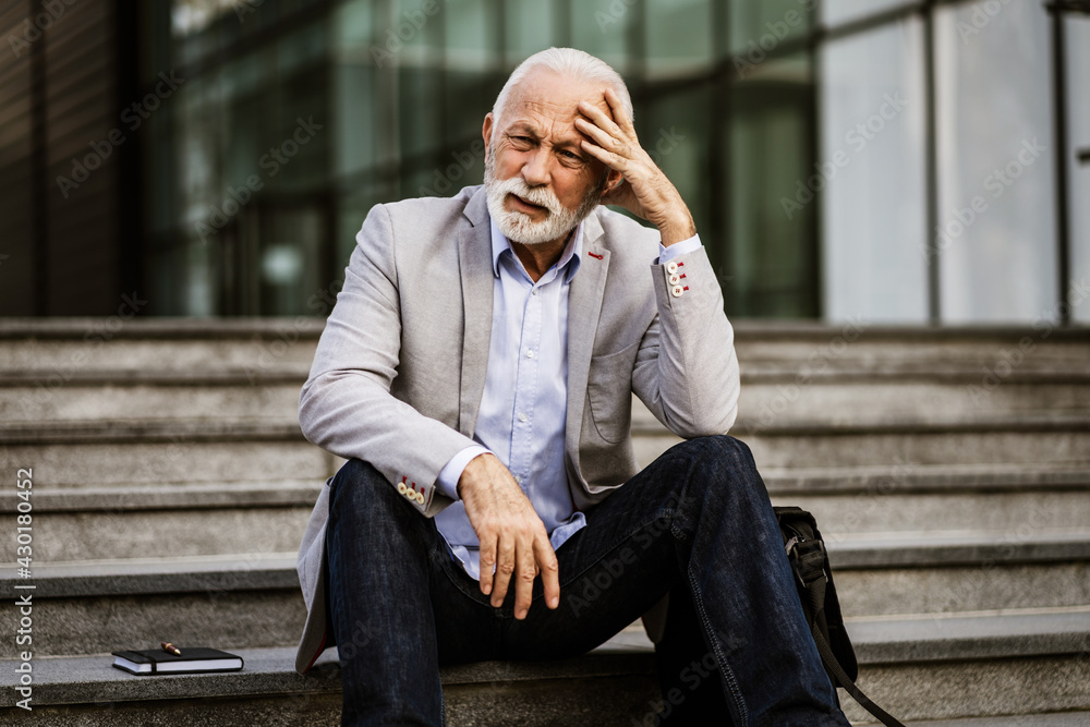 Senior businessman is tired of work. He is sitting in front of company building and having headache. Senior businessman is tired of work. He is sitting in front of company building and having headache.