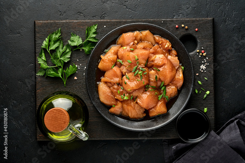 Foto Raw chicken meat marinated in teriyaki soy sauce, onions and pepper in a black plate on a dark slate, stone or concrete background