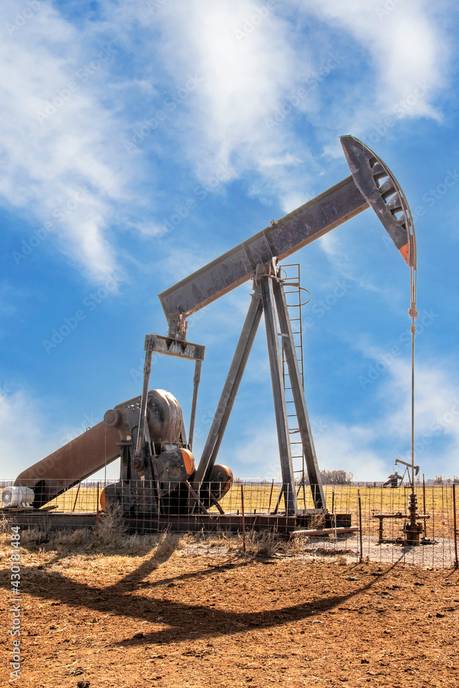 Oilfield pump jack out in summer red dirt field on bright day with shadow and a few whispy clouds in blue sky. Oilfield pump jack out in summer red dirt field on bright day with shadow and a few whispy clouds in blue sky.