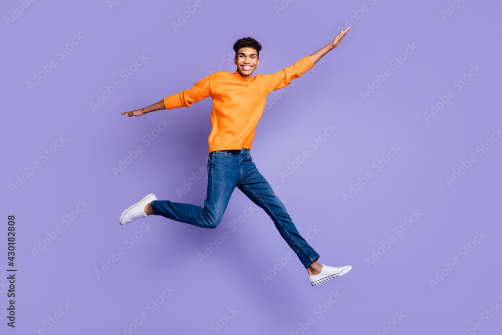 Full body photo of handsome dark skin man wear jeans jump go empty space hands wings isolated on purple color background