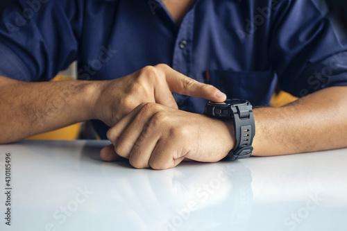 businessman wearing digital smart watch in hand touching screen to open notification, read message and activity tracker in wrist with soft-focus and over light in the background.