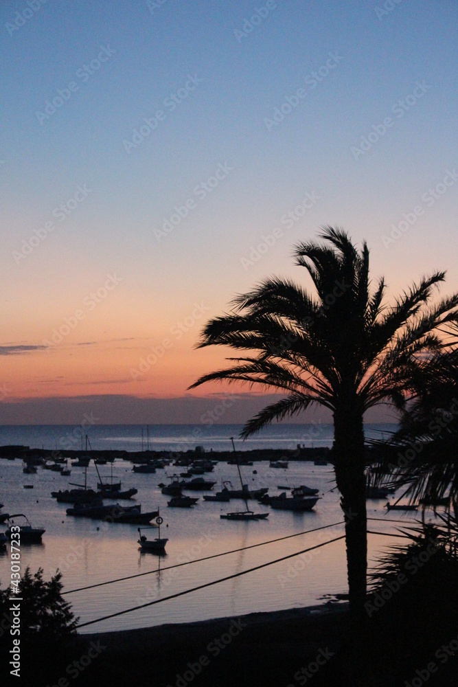 Obraz premium Golden sunset at a perfect vacation day in paradise, romantic feeling with palm trees and boats at the beach, golden heaven over the horizon, time to relax and leave problems behind