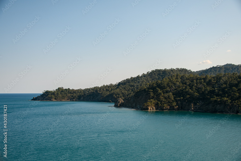 panoramic view of sea on background of mountain ranges with green trees and blue sky
