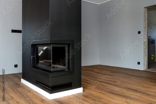A modern fireplace with a closed combustion chamber standing in the living room, painted black, with a corner pane covered with soot.