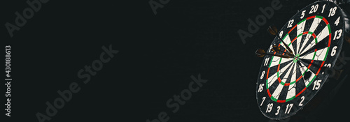 Quadro su tela Dartboard with dart arrow hitting on a dark black background with copy space