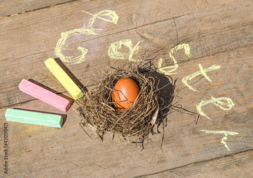 Easter egg in a coiled nest on a wooden background and the inscription "Easter" with colored crayons.
