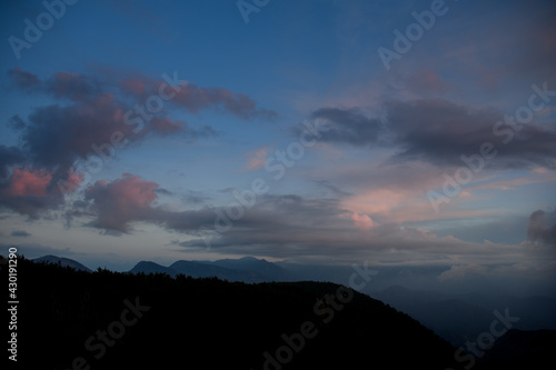 glamorous sky with vivid clouds. Dark silhouettes of mountains and trees at dawn.