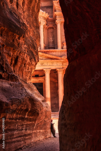View of the Treasury from the narrow canyon of the Sin. An arab person in leaning in the wall at the end of the way 