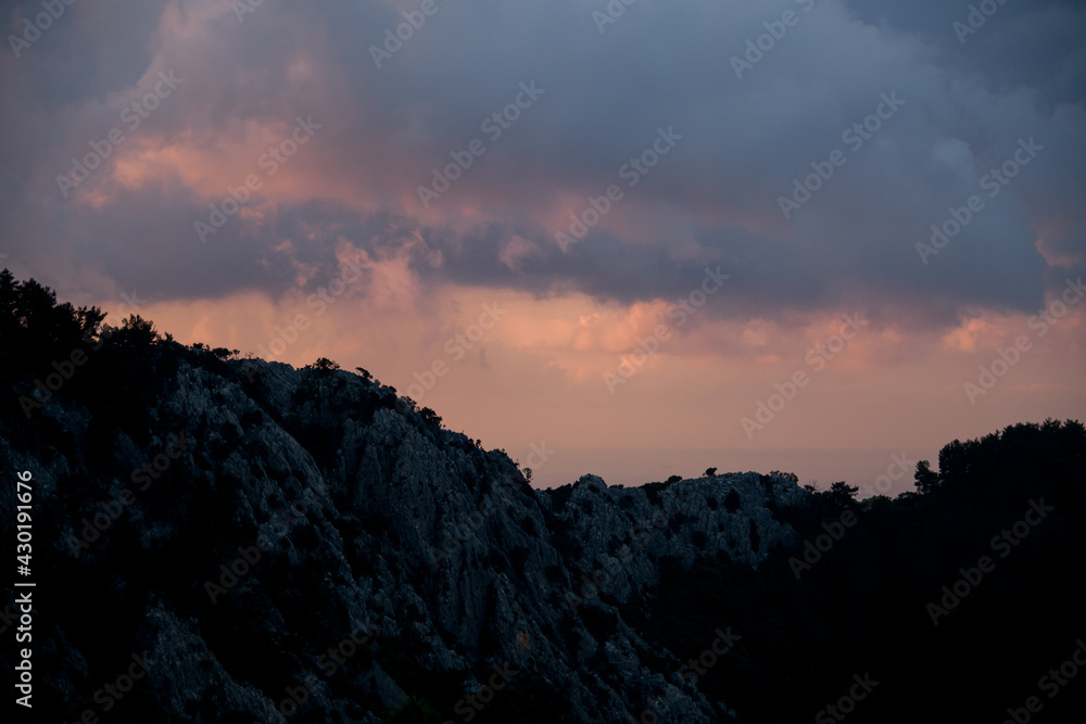 Majestic view on sky and clouds at sunrise. Dark silhouettes of mountains at dawn.