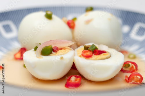 Close up view. Boiled eggs in a plate cut in two halves with yolk inside with poured fresh chili sauce.