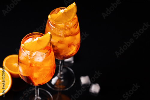 Glasses of ice cold Aperol spritz cocktail served in a wine glass, decorated with slice of orange, black mirrow background, close up, space for text