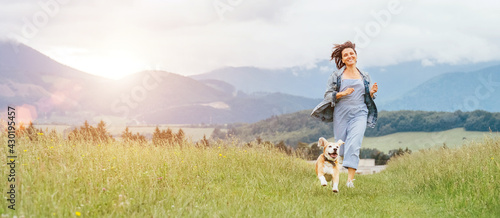Happy smiling running beagle dog portrait with tongue out and owner female jogging by the mounting meadow grass path. Walking in nature with pets, happy healthy active people lifestyle concept image.