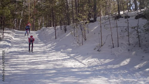 Professional biathletes with poles and rifles skiing downhill while racing on cross country trail photo