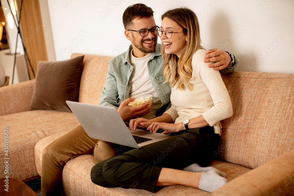 Young couple using laptop together while sitting on sofa at home Young couple using laptop together while sitting on sofa at home
