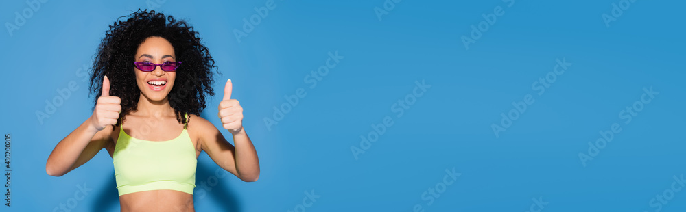 happy african american woman in sunglasses showing thumbs up on blue, banner happy african american woman in sunglasses showing thumbs up on blue, banner