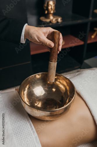 Tibetan singing bowls on the belly and hand. Sound massage with singing bowls on the body. Vibrational therapy. Woman doing relaxing massage, meditation. Stress relief. Spa with Buddha decoration.