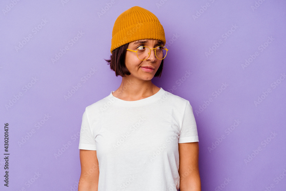 Young mixed race woman wearing a wool cap isolated on purple background confused, feels doubtful and unsure.