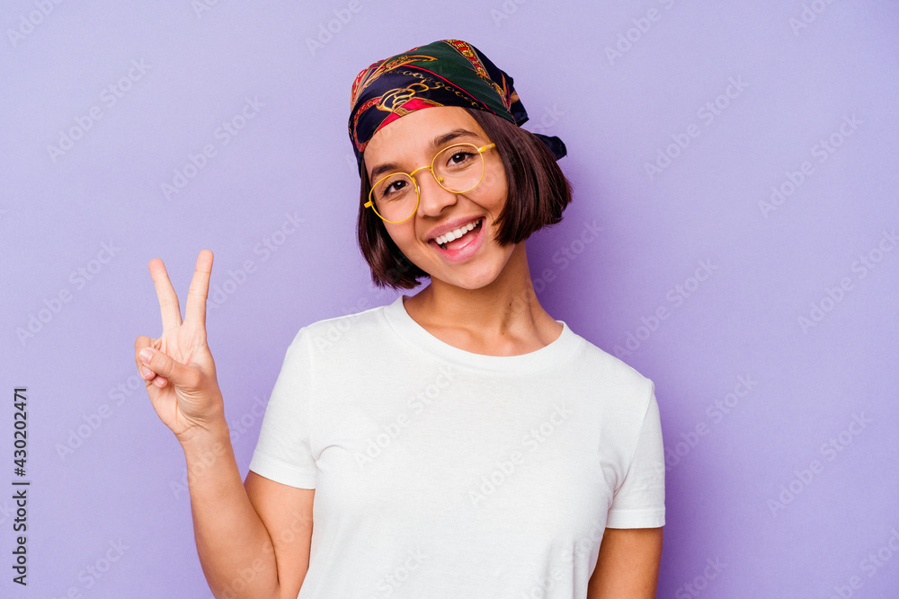 Young mixed race woman wearing a bandana isolated on purple background joyful and carefree showing a peace symbol with fingers.